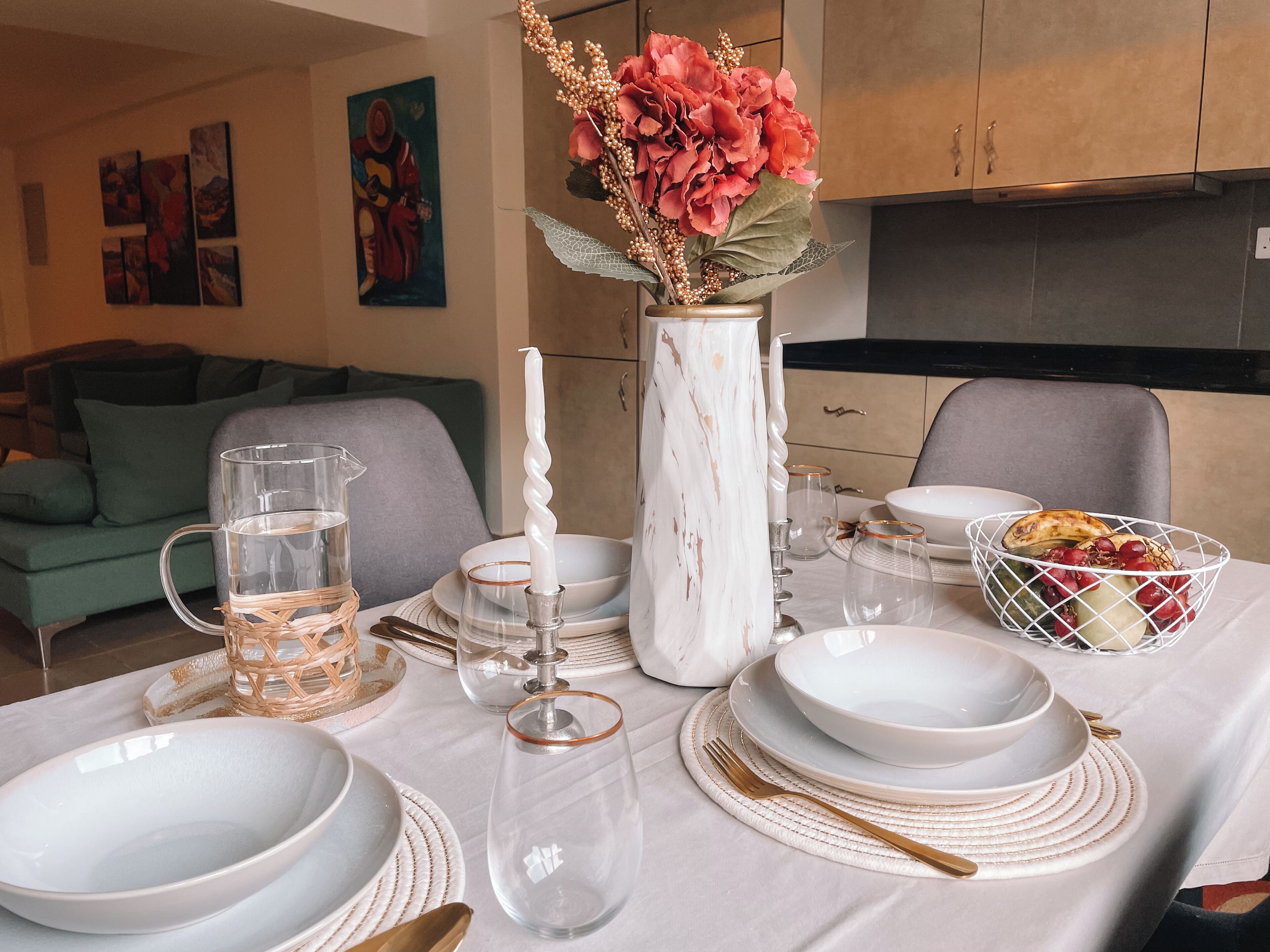 A dining table set with white plates, bowls, and cutlery, a vase with flowers, and a pitcher of water.