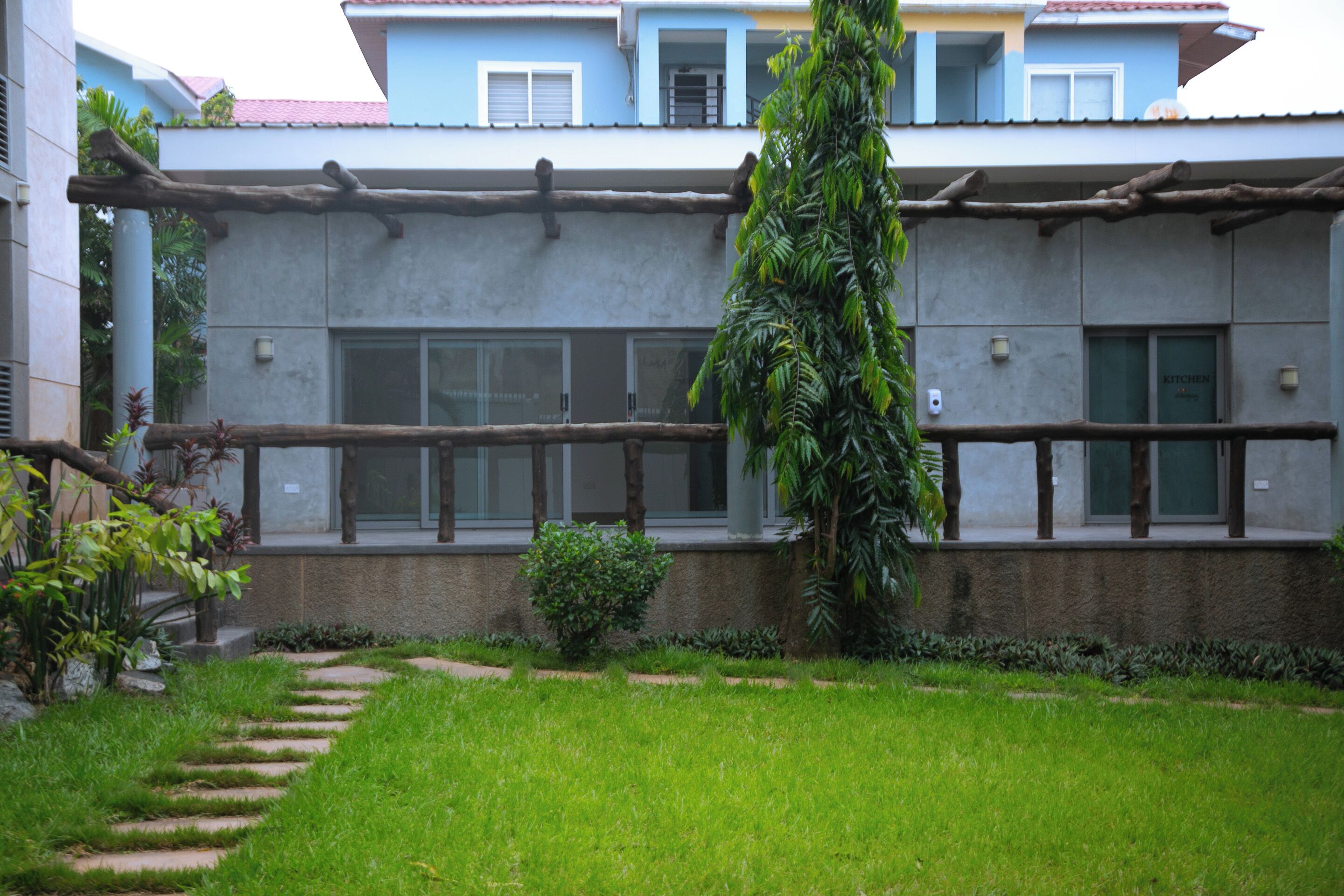 Ein Gebäude mit einer Betonfassade, einer Holzpergola und einem gepflegten Rasen mit einem Kiesweg.