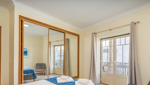 Une chambre d’hôtel avec un lit, une chaise, un grand miroir et un balcon avec des rideaux.
