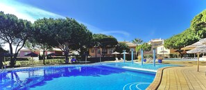 A swimming pool with a tiled deck, surrounded by trees and buildings.