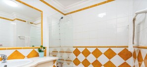 A bathroom with white tiles, a glass shower enclosure, and a sink with a mirror.
