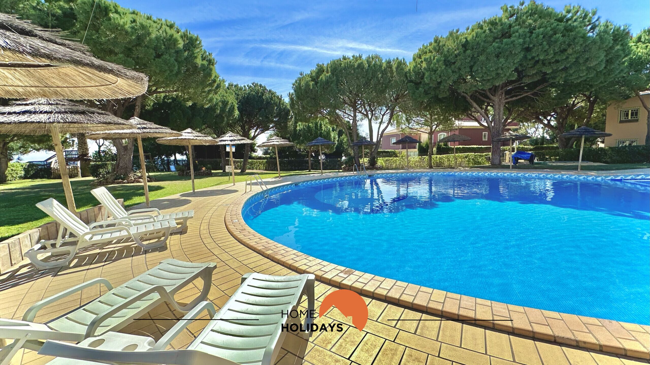 A swimming pool with lounge chairs and umbrellas, surrounded by trees and buildings.