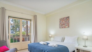 Una habitación de hotel con una cama, una silla, una mesita de noche, una lámpara y una ventana con cortinas.