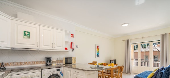 A compact kitchen with a washing machine, microwave, and coffee maker. - #273 Pedra dos Bicos M by Home Holidays (Albufeira)