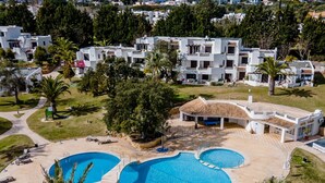 Un resort con varias construcciones, un área de piscina central y una zona de estar al aire libre techada.