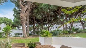 Un patio con una mesa y sillas, rodeado de árboles y un edificio blanco al fondo.