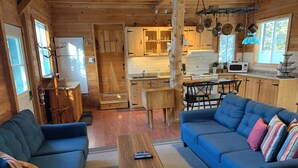 Interior acollidor d'una cabana amb saló, sofà, taula de café, i zona de cuina amb armaris de fusta i taula de dinar.