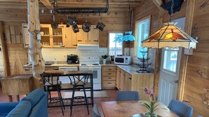 Interior acollidor d'una cabana de fusta amb menjador, cuina i una finestra gran.