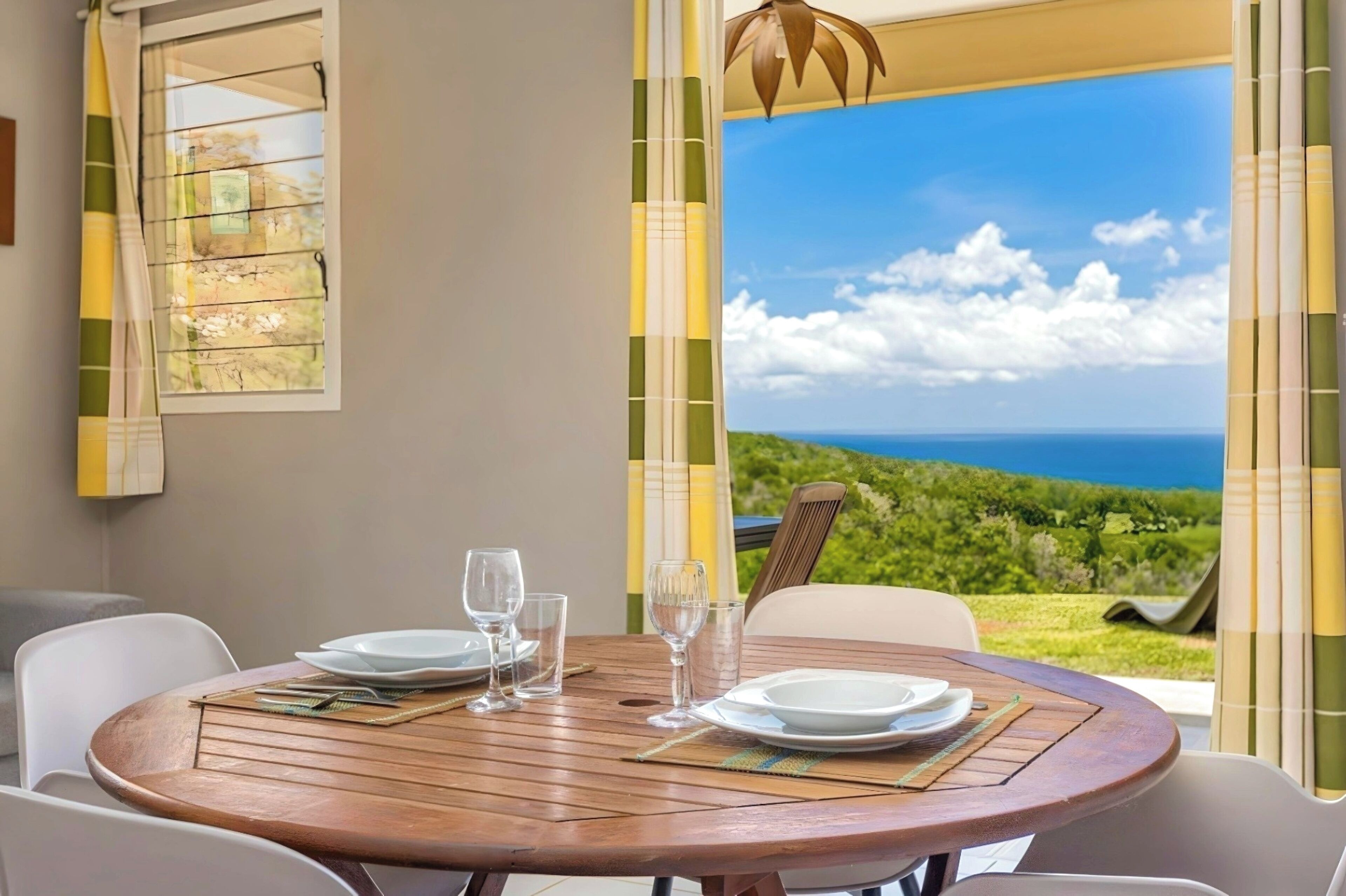 A dining table with plates, glasses, and a view of a lush landscape through a window.