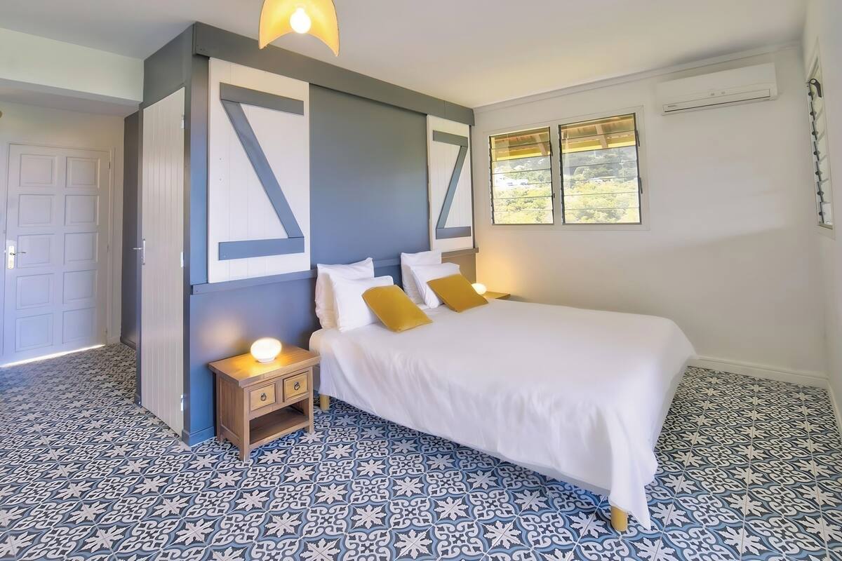 Ein Schlafzimmer mit Bett, Nachttischen, einem Fenster mit Blick und Fliesenboden.