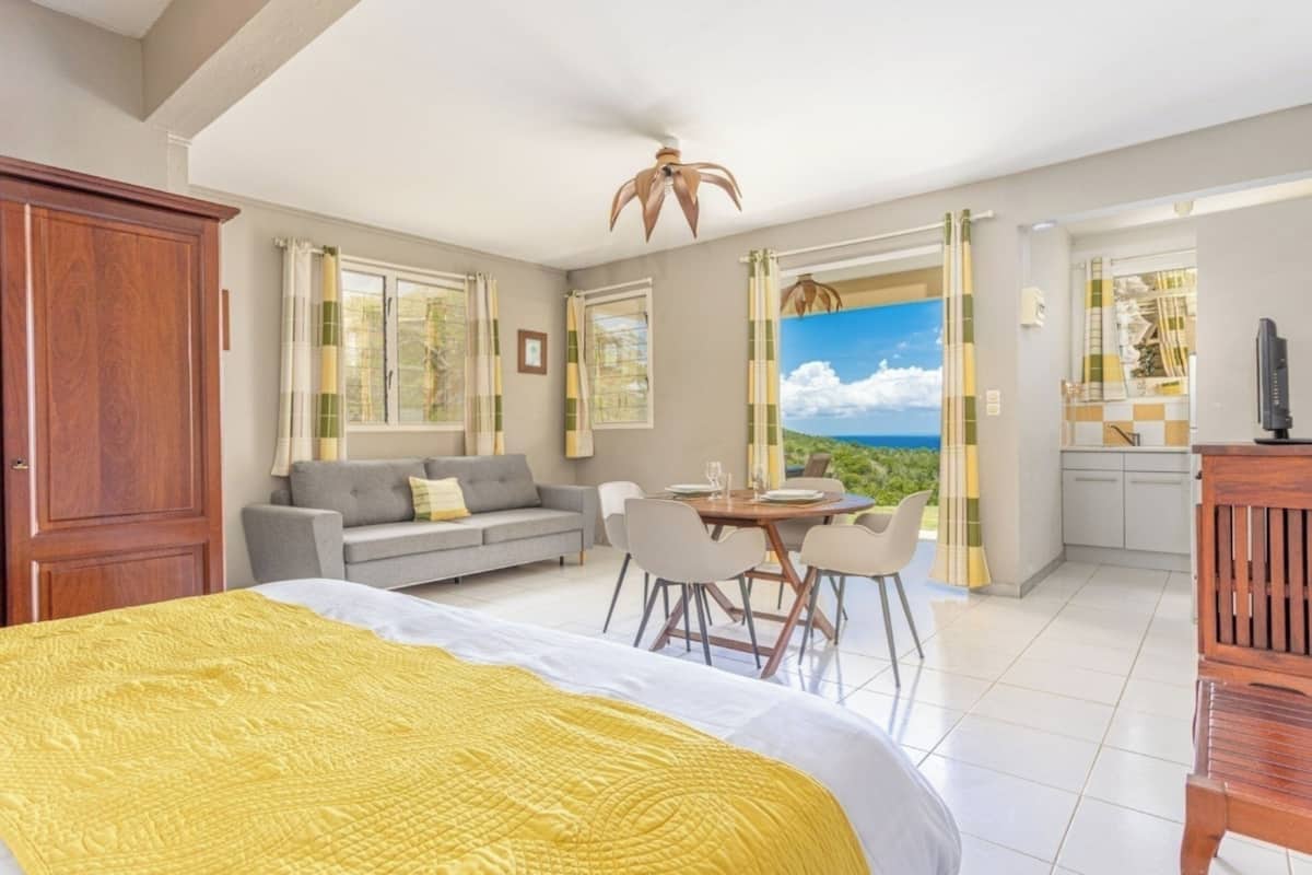 Ein Schlafzimmer mit Bett, Sofa, Esstisch und Stühlen sowie Blick aufs Meer.