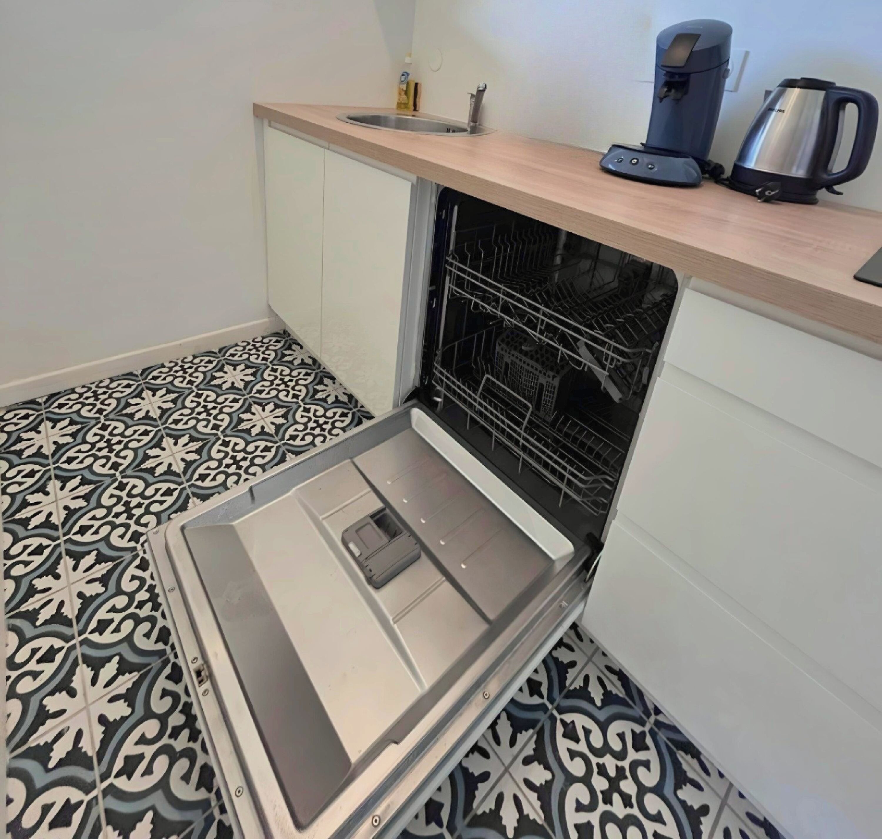 Una cocina con lavavajillas, cafetera y hervidor sobre la encimera.