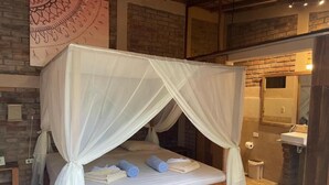 Un lit doté d’un baldaquin blanc, d’une tête de lit en bois et de serviettes enroulées posées sur le matelas.