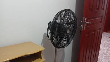 Une pièce avec un ventilateur sur pied, une table en bois et une porte rouge.