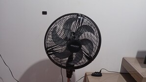 A standing fan with a power cord, placed on a patterned floor next to a wooden cabinet. - Beautiful and cozy house, spacious and close to the center (Boa Esperança Toledo)