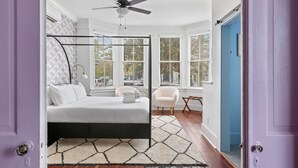 Una camera da letto con un letto a baldacchino, una ventola a soffitto e vista esterna attraverso ampie finestre.