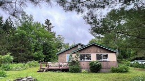 Un chalet rustique aux murs en bois et au toit vert, entouré d’une végétation luxuriante et d’arbres.