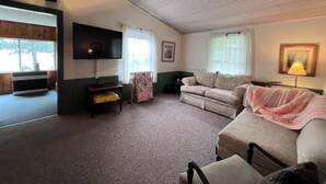 A living room with a flat-screen TV, a sofa, a chair, a table, and a lamp.