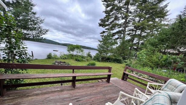 Une terrasse en bois avec des chaises et un banc en osier, donnant sur un lac.
