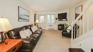 A living room with a leather sofa, a TV, a fireplace, and a staircase.