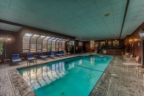 Une piscine intérieure dotée de chaises longues, d’un bar et offrant une vue à travers une paroi vitrée.