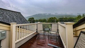 A covered outdoor area with a wooden deck, a railing, and a view of a mountainous landscape.