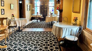 A dining area with a patterned floor, tables with white tablecloths, and chairs. - Ruby Room -The Amethyst Inn Bed & Breakfast- jacuzzi tub, fireplace, breakfast (Adamstown)