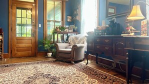 A room with a wooden door, large windows, a patterned rug, a chair, a dresser, and a lamp. - Ruby Room -The Amethyst Inn Bed & Breakfast- jacuzzi tub, fireplace, breakfast (Adamstown)