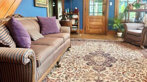 A cozy living room with a striped sofa, a patterned rug, and a wooden staircase. - Ruby Room -The Amethyst Inn Bed & Breakfast- jacuzzi tub, fireplace, breakfast (Adamstown)