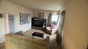 Un salon avec un canapé, un téléviseur, une petite table et une chaise.