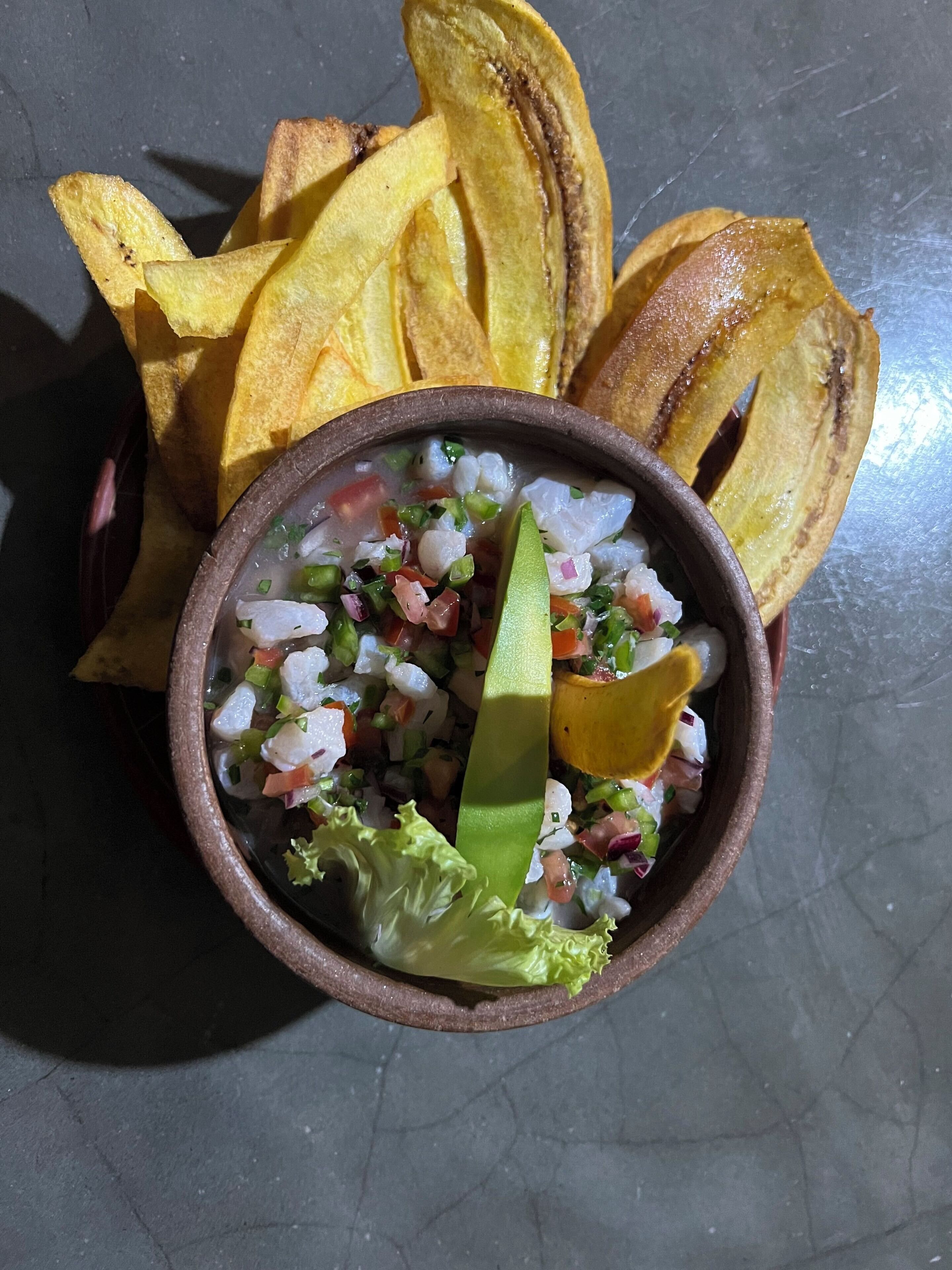 A bowl of ceviche with avocado and lime, accompanied by fried plantains.