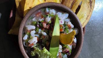 A bowl of ceviche with avocado and lime, accompanied by fried plantains.