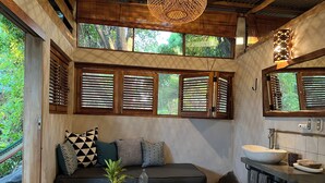 A cozy room with a sofa, a wooden table, a sink, and large windows with wooden shutters.
