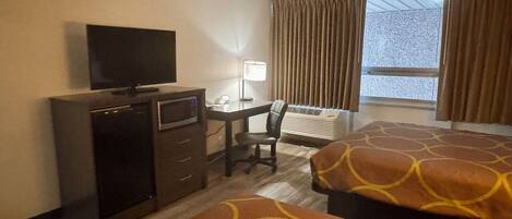A hotel room with a desk, a television, a chair, two beds, a heater, and a window with curtains.