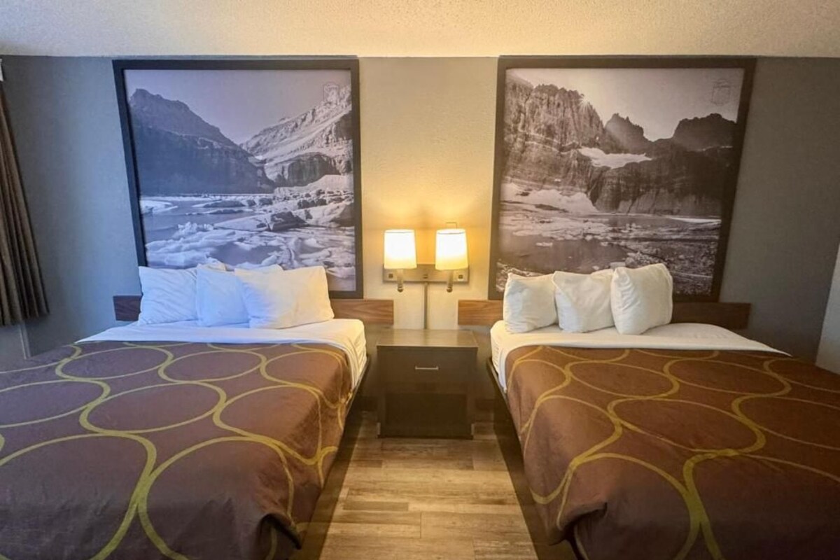 A hotel room with two beds, a wooden floor, and two wall-mounted lamps.