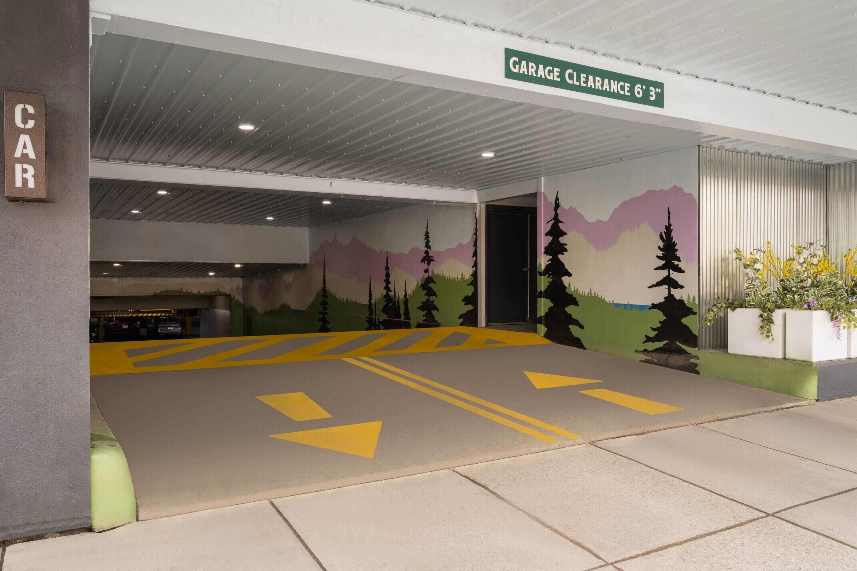 A parking garage with a clear height limit sign, directional arrows on the floor, and a mural on the wall.