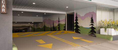 A parking garage with a clear height limit sign, directional arrows on the floor, and a mural on the wall.