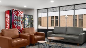 A lobby with leather sofas, a Coca-Cola vending machine, a beverage dispenser, and large windows with a view of a building. - Super 8 By Wyndham Great Falls City Center (Great Falls)