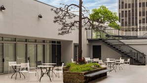A modern outdoor seating area with white tables and chairs, a stone planter with greenery, and a staircase leading to an upper level. - Super 8 By Wyndham Great Falls City Center (Great Falls)