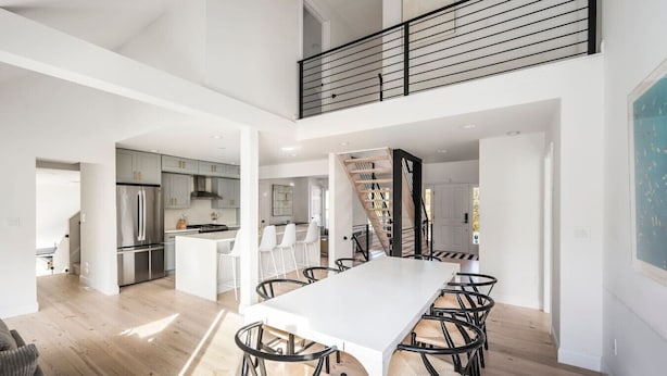 Una cocina amplia y moderna con una isla central, un comedor con una mesa grande y sillas, y una escalera que sube a un nivel superior.