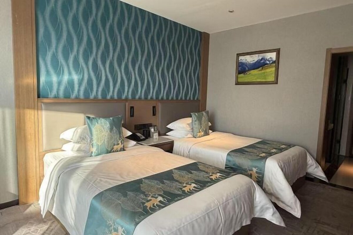 A hotel room with two beds, a large window, a painting on the wall, and a wooden headboard.