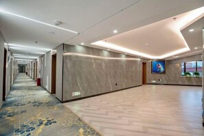 A hotel corridor with a patterned carpet, a large flat-screen TV, and a wall-mounted TV. - Holiday Inn Altay Golden Bridge (Altay City)