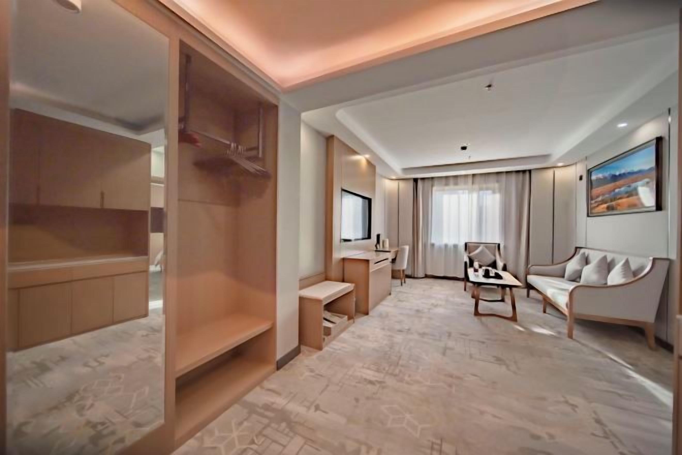 Una habitación de hotel moderna con vestidor, escritorio con silla, sofá y un ventanal con cortinas.