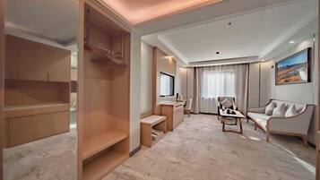 Una habitación de hotel moderna con vestidor, escritorio con silla, sofá y un ventanal con cortinas.