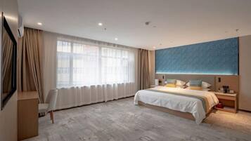 Una habitación de hotel moderna con una cama grande, un escritorio y un amplio ventanal con cortinas.