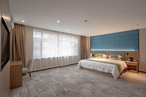 Una habitación de hotel moderna con una cama grande, un escritorio y un amplio ventanal con cortinas.