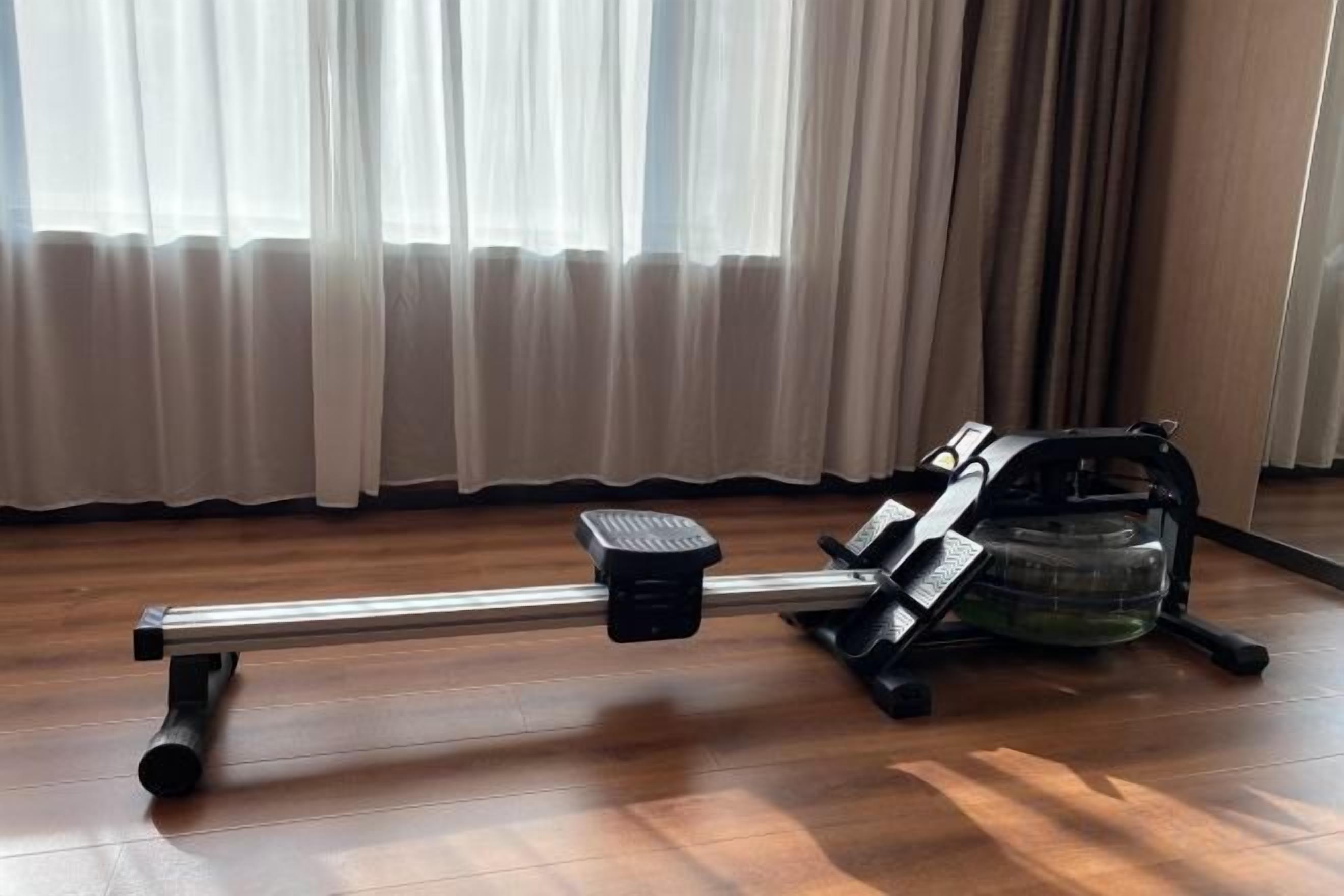 A stationary exercise bike in a room with wooden flooring and a window with curtains.