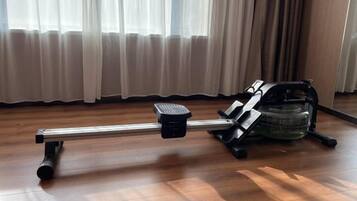 A stationary exercise bike in a room with wooden flooring and a window with curtains.