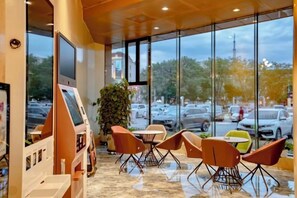 A restaurant with a self-service kiosk, outdoor seating with chairs, and a view of the street through large windows. - Holiday Inn Altay Golden Bridge (Altay City)