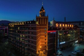 Un hotel de varios pisos con una destacada torre de reloj, un área de estacionamiento y vistas de la ciudad circundante.